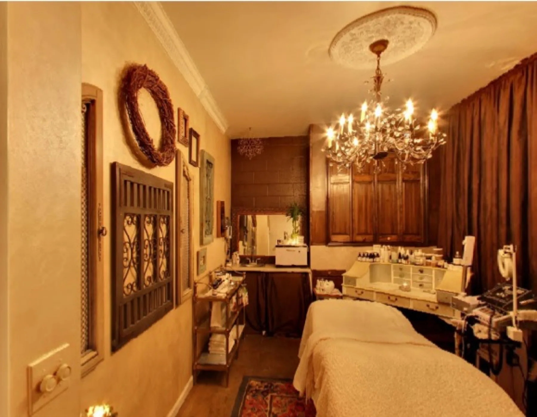 A warm, candlelit treatment room at our Aspinwall spa, with a dressed treatment bed beneath a crystal chandelier