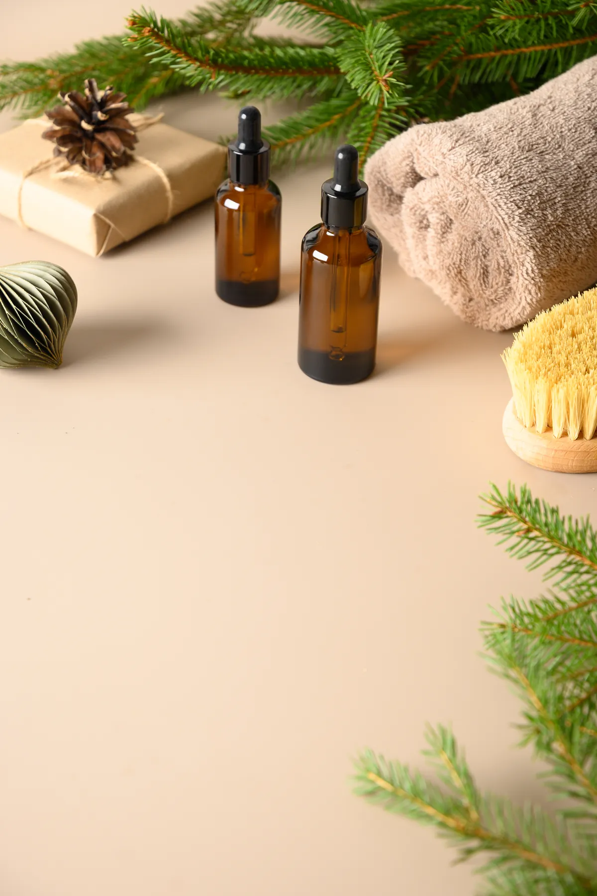 Holiday spa gift set with amber skincare oils, a wrapped gift box, a rolled towel, and fir branches