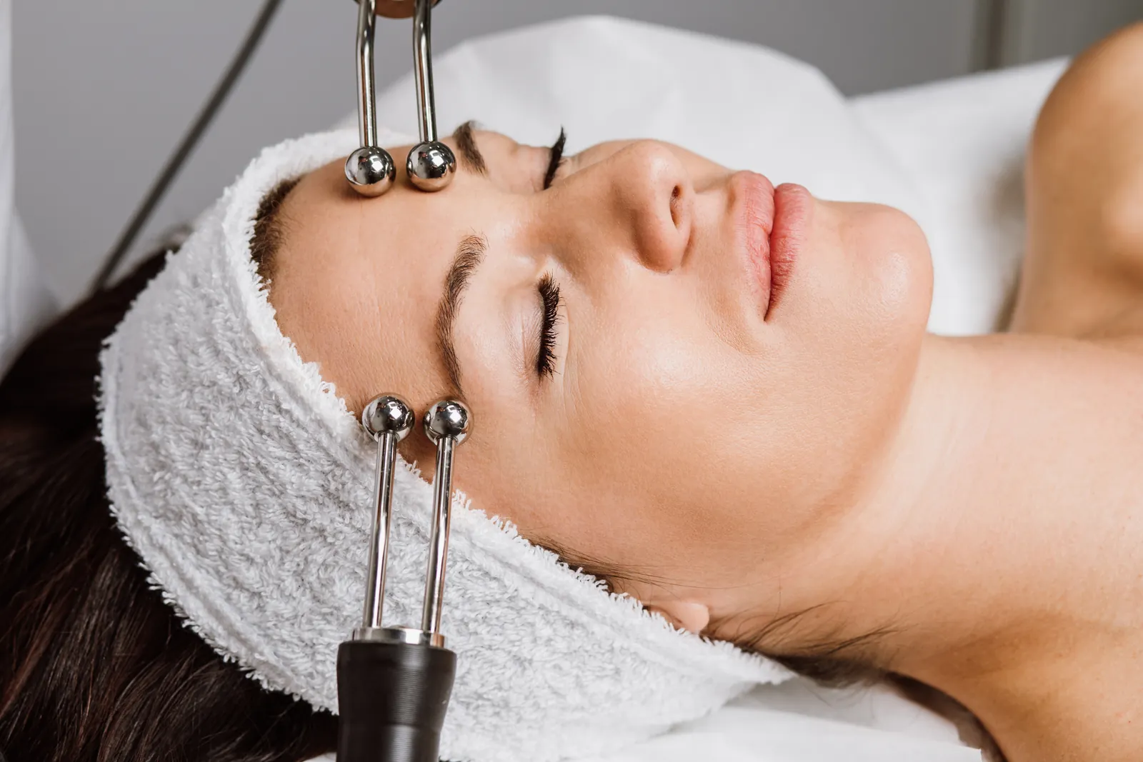 Guest receiving a microcurrent facial with twin metal probes along the brow and cheek