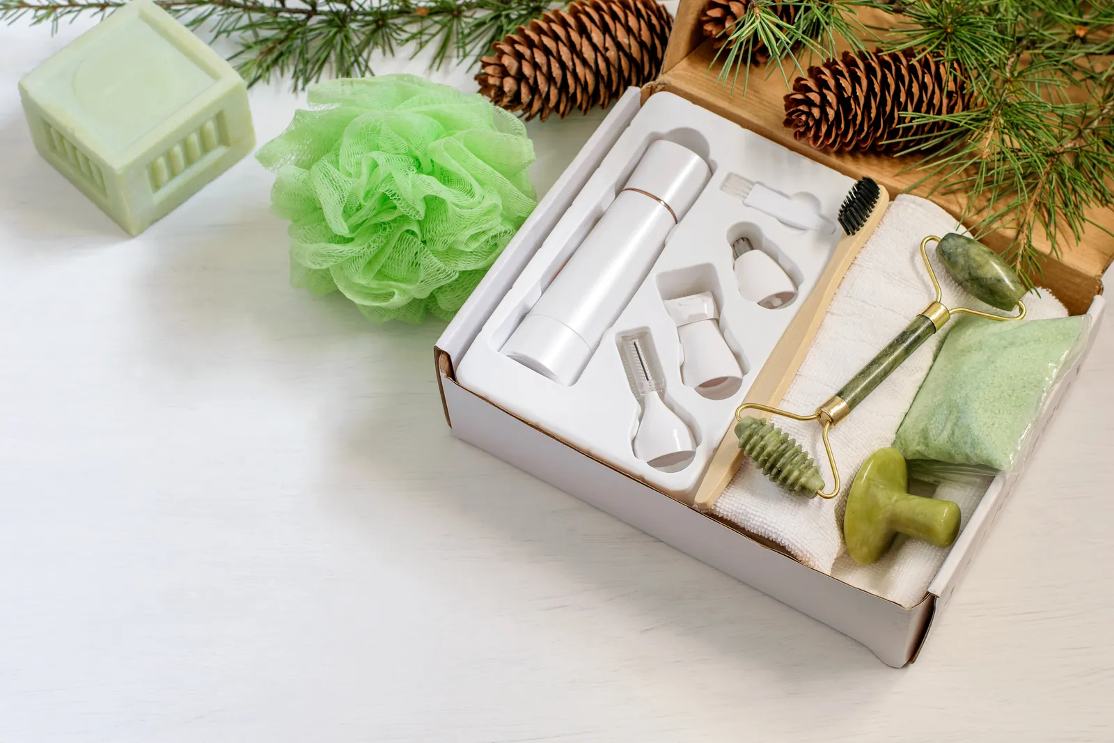 Spa gift box with a jade roller, a gua sha stone, and skincare tools beside pine cones and fir branches